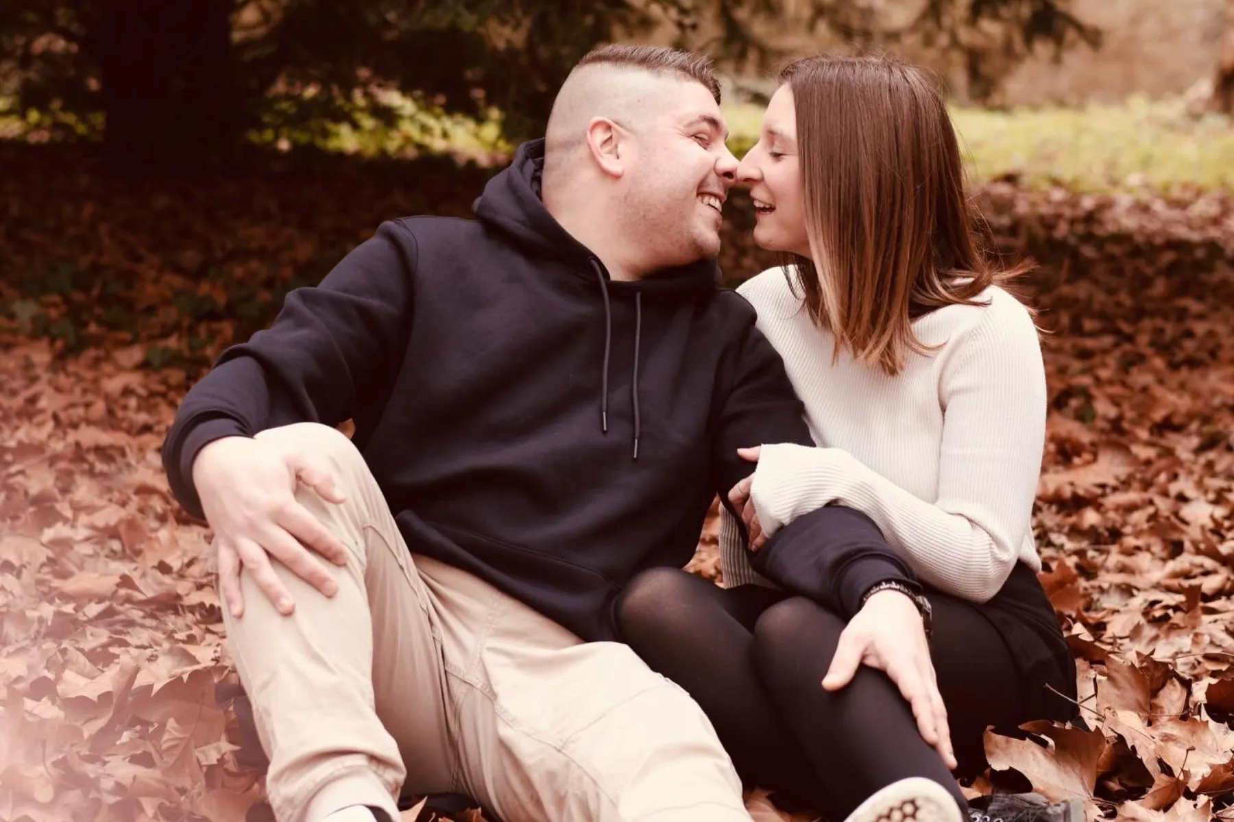 Un couple assis dans les feuilles d'automne, nez contre nez