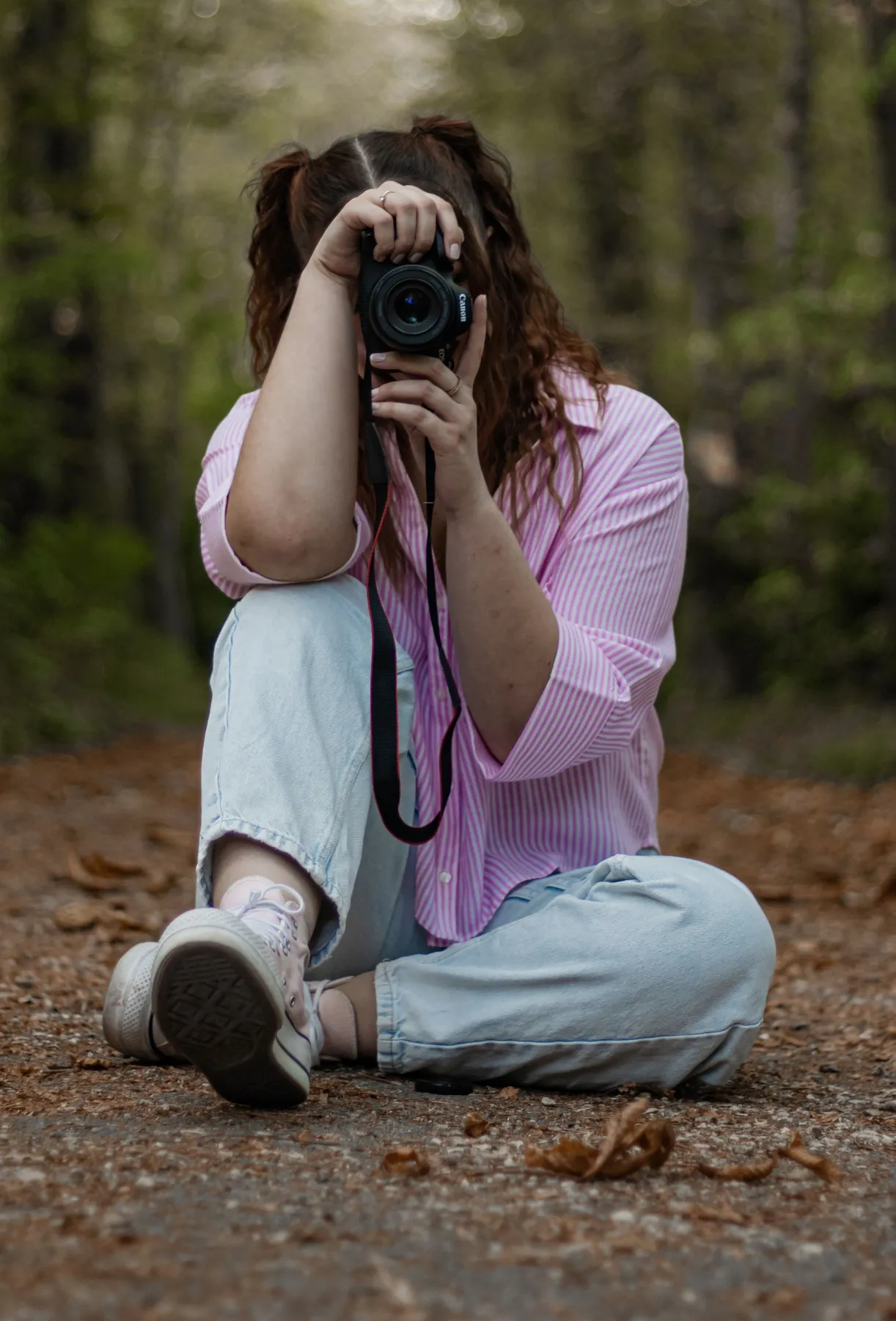 Marion, assise sur un chemin forestier, vise l'objectif vers vous