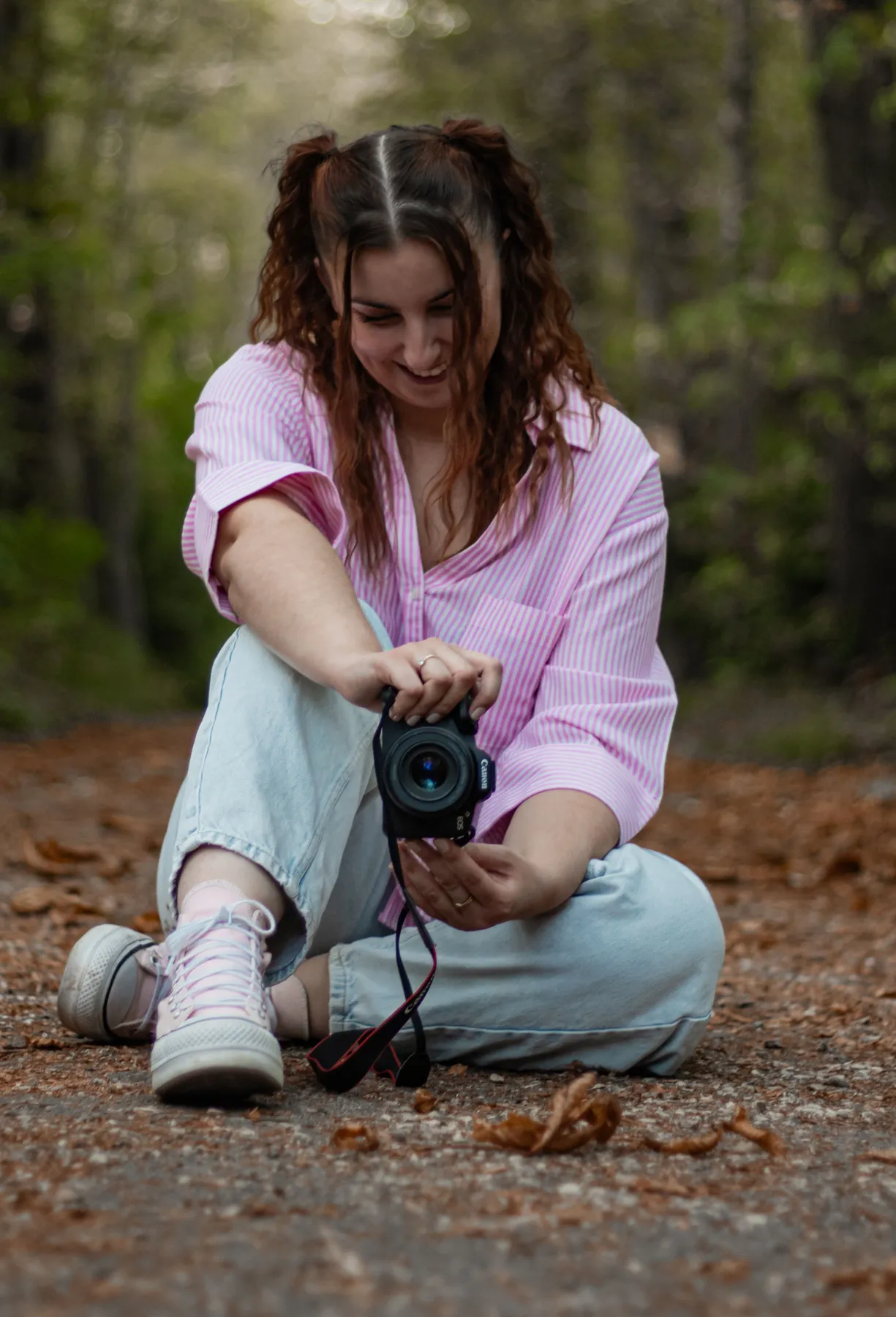 Marion sourit en regardant son appareil, assise sur un chemin en forêt