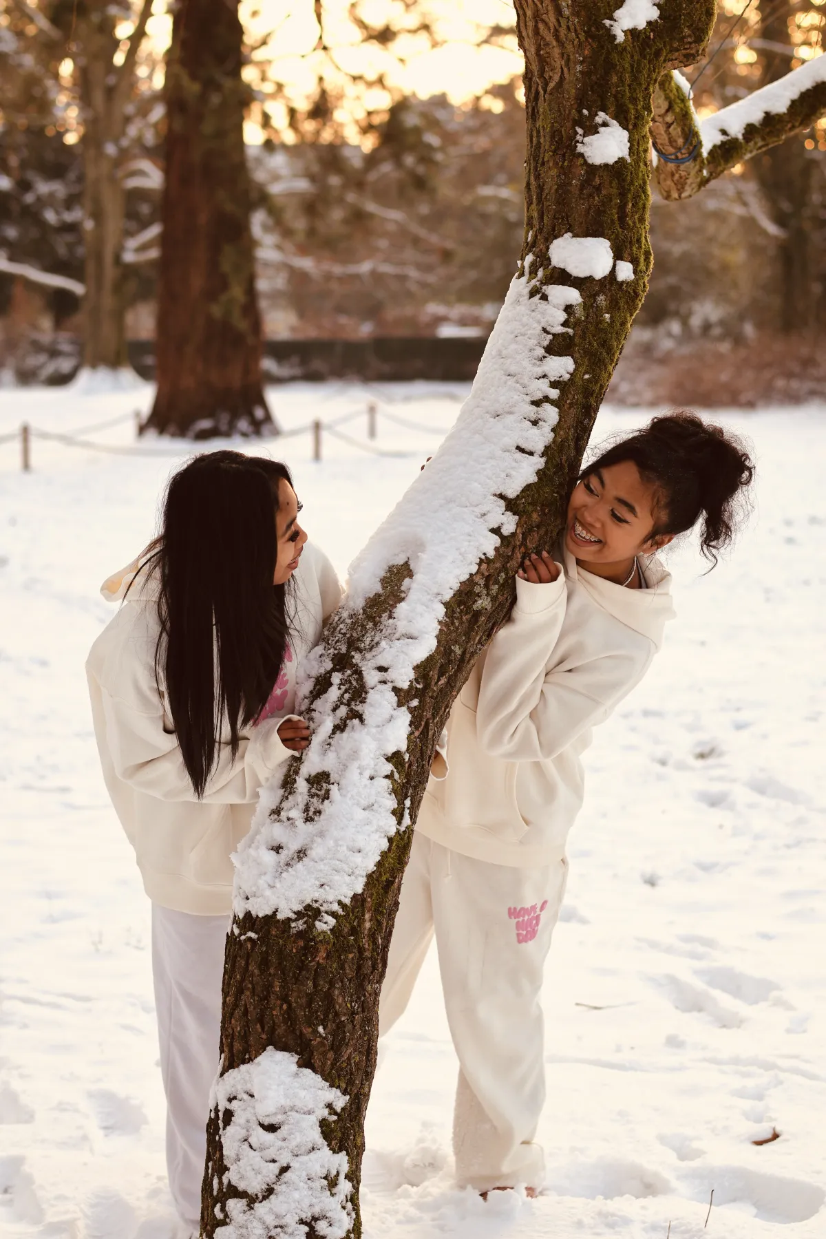 Deux fillettes rient derrière un arbre enneigé