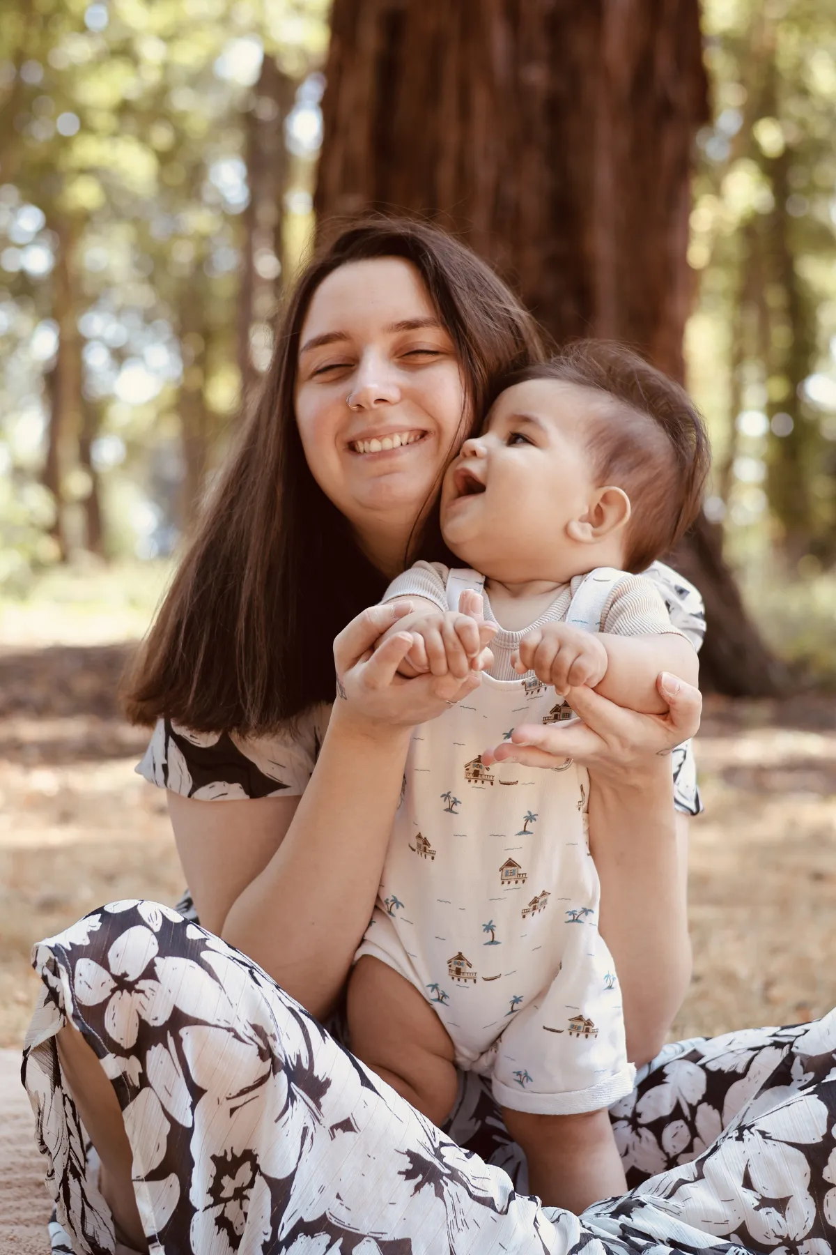 Une maman rit avec son bébé dans un sous-bois ensoleillé
