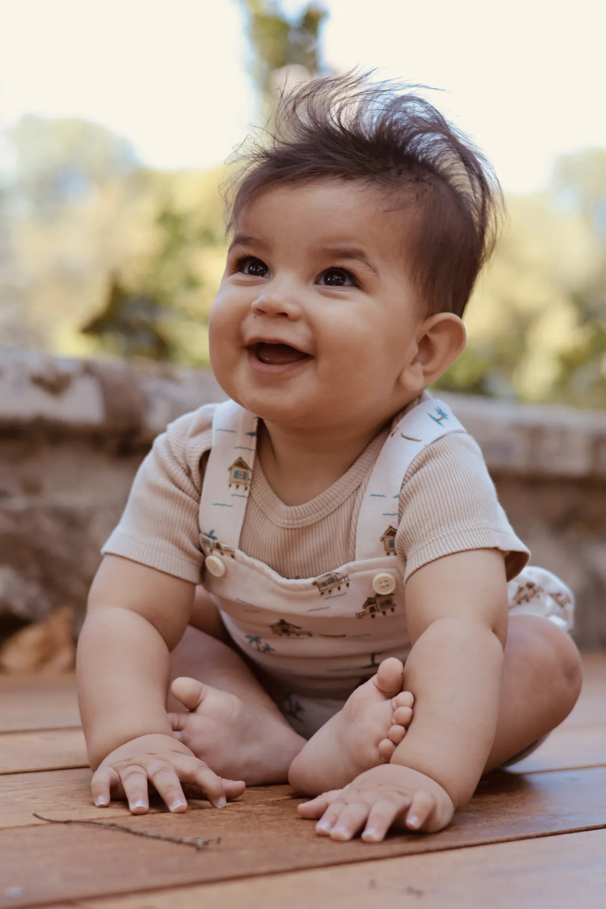 Un bébé souriant assis sur une terrasse en bois