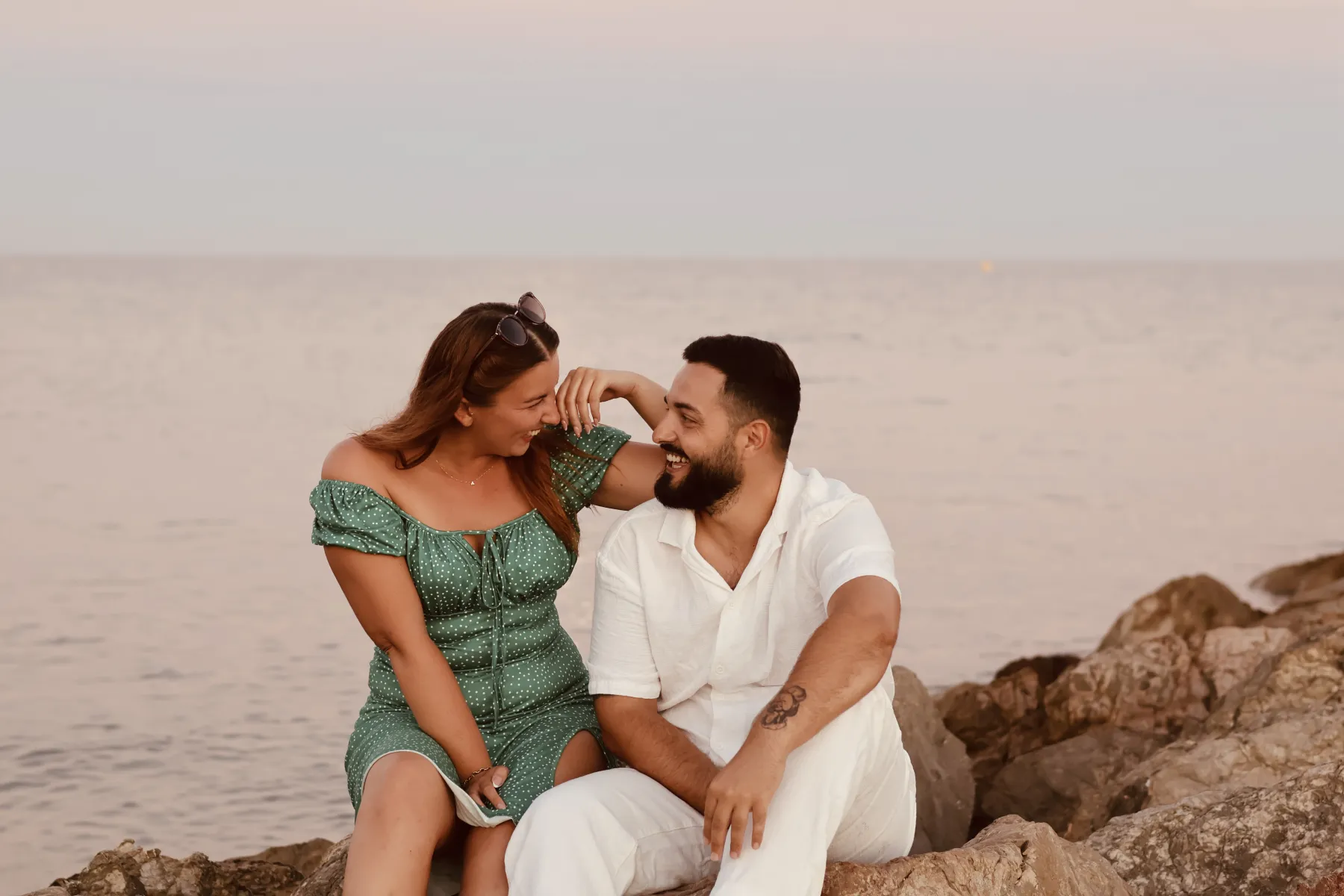 Un couple complice assis sur les rochers face à la mer