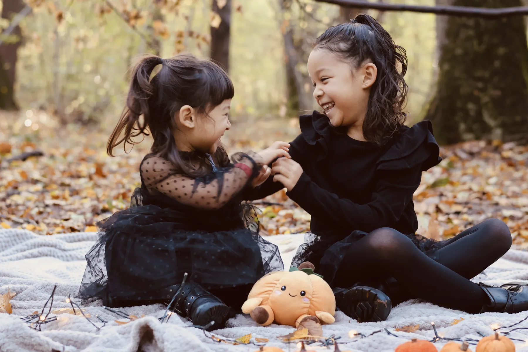 Deux fillettes en tenue d'Halloween rient main dans la main dans les feuilles mortes