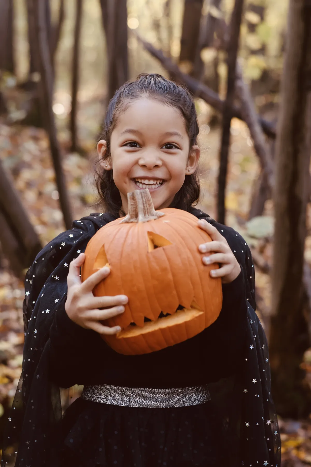 Une fillette en cape étoilée sourit, une citrouille d'Halloween dans les mains