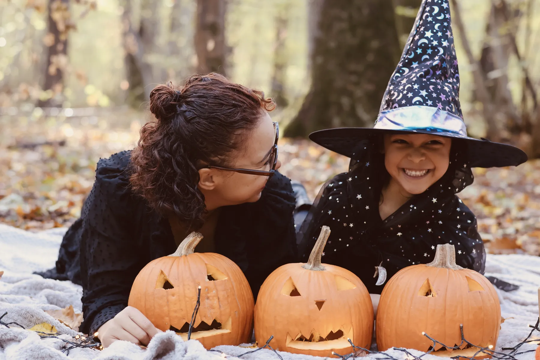 Une maman et sa fille déguisée en sorcière, allongées derrière trois citrouilles d'Halloween