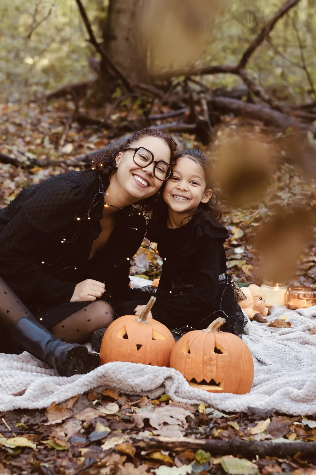 Une maman et sa fille blotties derrière des citrouilles en forêt