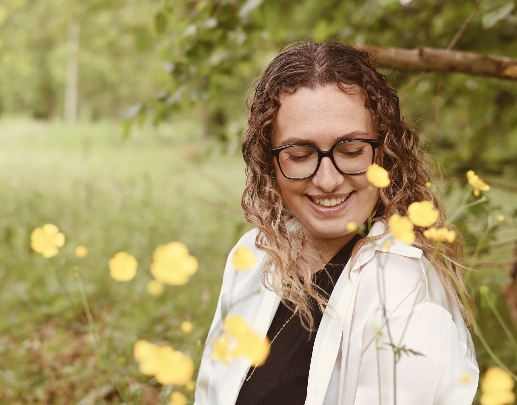 Jeune femme aux cheveux bouclés souriante parmi des boutons d'or