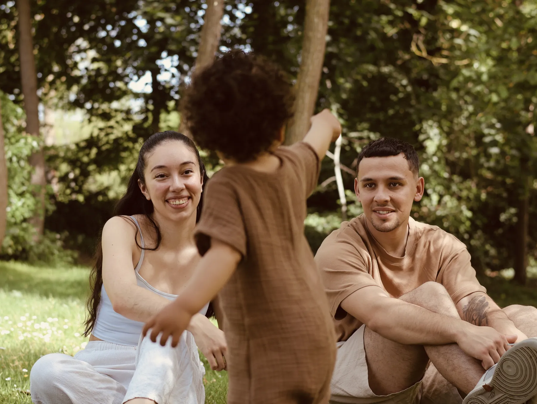 Des parents assis dans l'herbe accueillent leur enfant qui marche vers eux