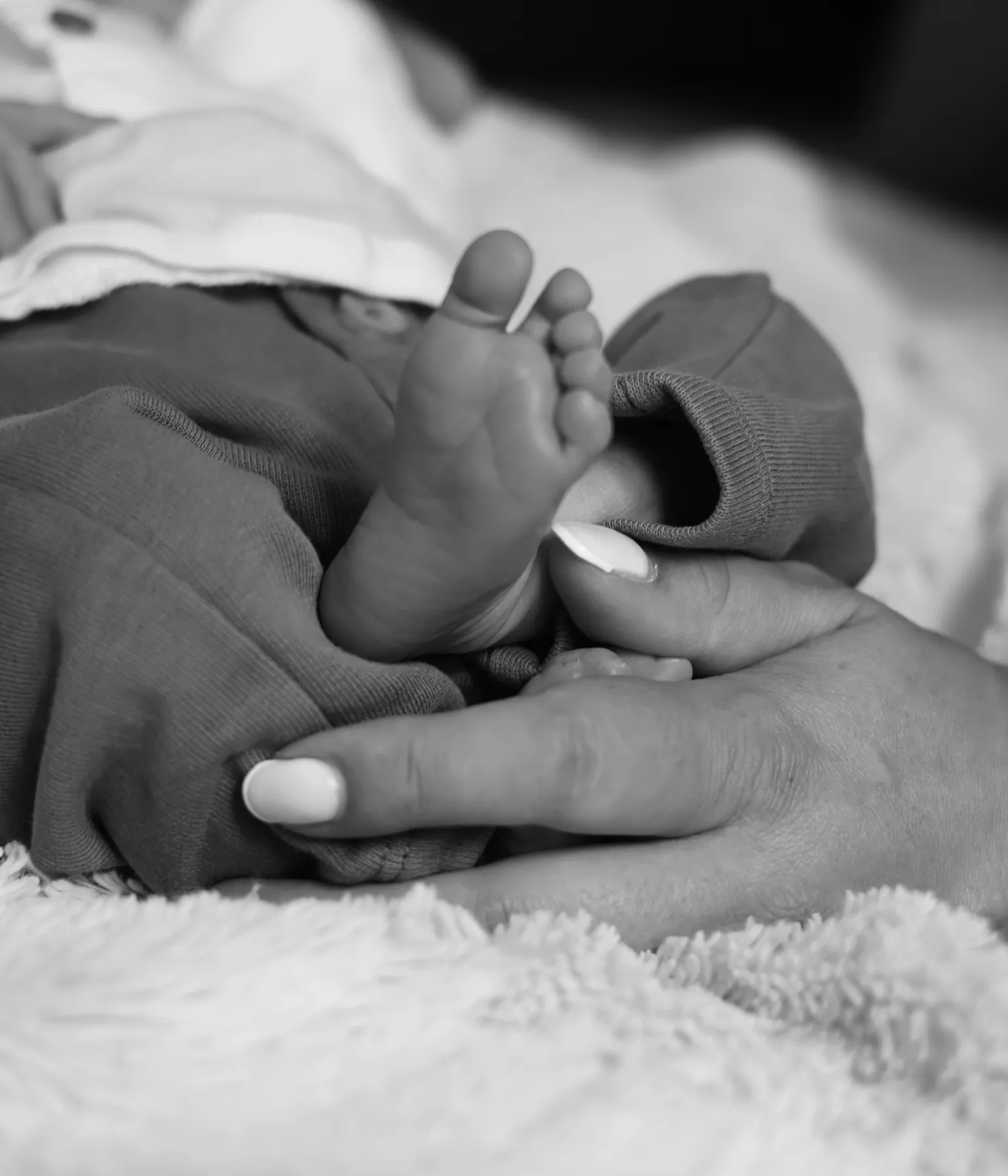 Le pied d'un nouveau-né dans la main de sa maman, en noir et blanc