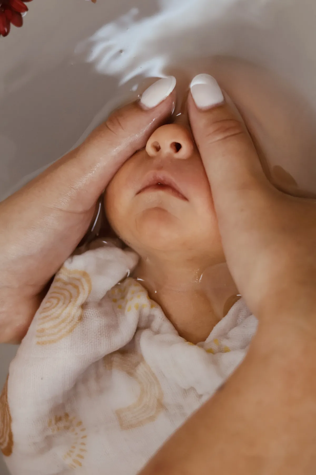Des mains soutiennent le visage d'un bébé pendant le bain enveloppé