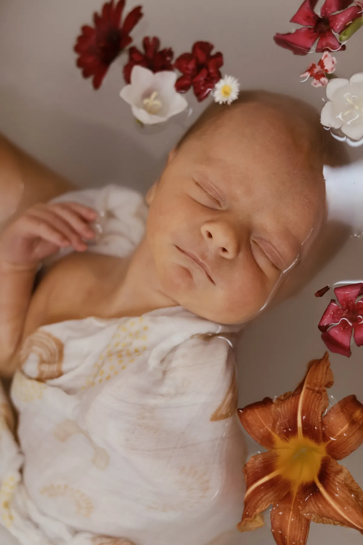 Nouveau-né endormi et emmailloté dans un bain parsemé de fleurs