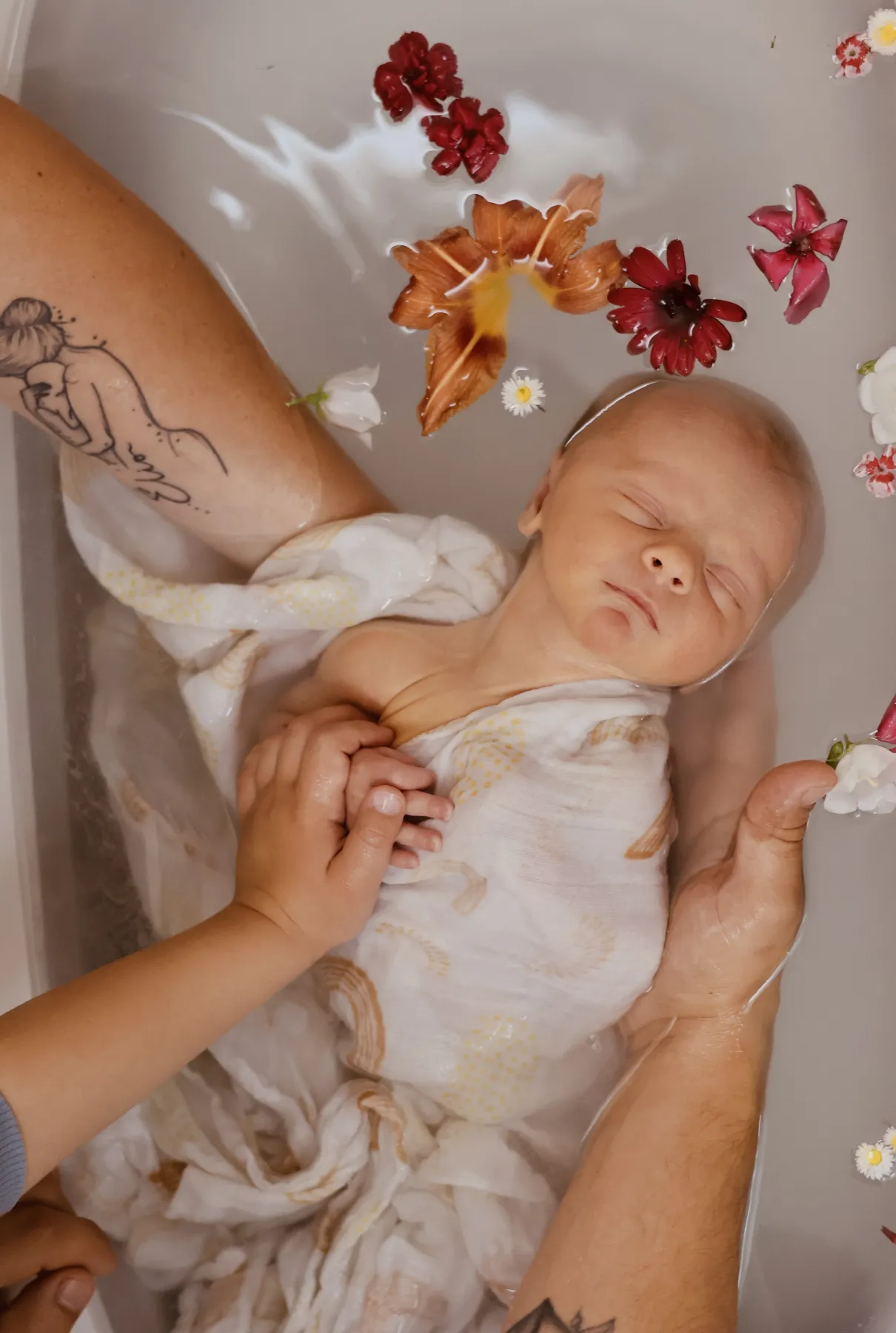 Bébé emmailloté dans le bain, tenu par les mains de ses parents